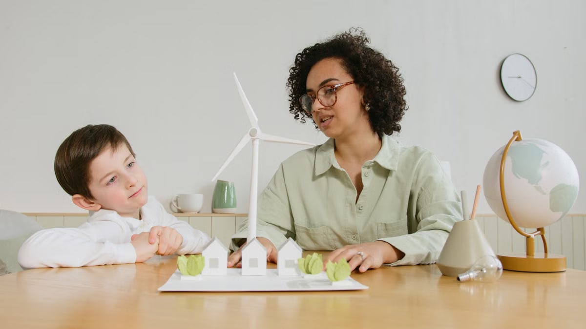 A child and teacher explore renewable energy concepts with a wind turbine model indoors.